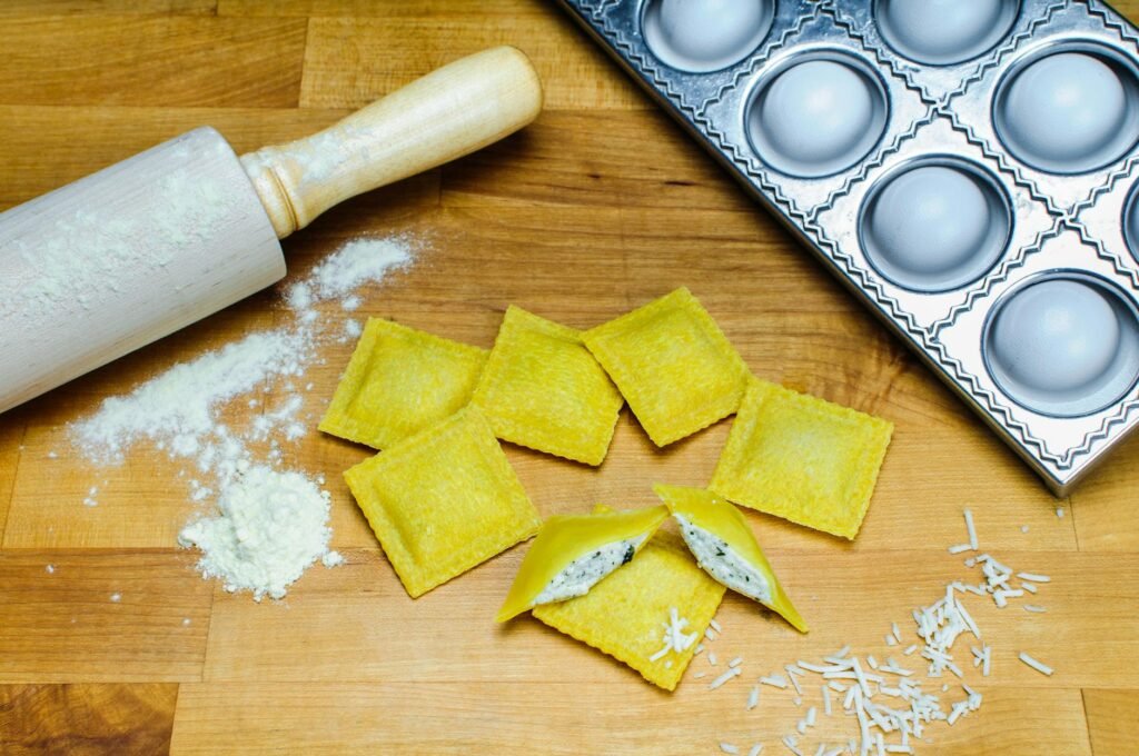 pexels-photo-5930586-5930586 Close-up of fresh homemade ravioli with rolling pin and mold on a wooden board.